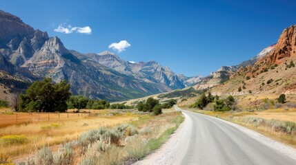 A dusty gravel road leads the way through a stunning canyon landscape, flanked by rugged mountains, under a bright blue sky with scattered clouds, showcasing natural beauty.