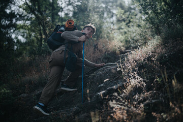 Solo hiker ascending a steep rocky trail in a dense forest. Adventurous outdoor activity and...