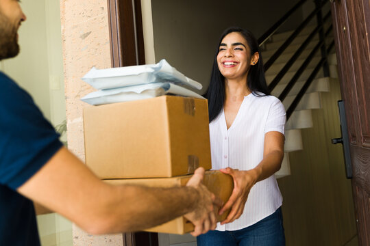 Hispanic woman accepting a pile of packages from a delivery man at her doorstep