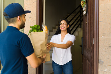Happy Latin woman accepting a grocery bag from a delivery man at her doorstep