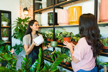 Hispanic worker is showing different pots to a customer who is buying a plant in a plant shop