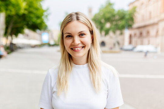 Fototapeta Smiling portrait of young caucasian woman looking at camera standing at city street. Joyful millennial girl feeling positive, closeup outdoor headshot. Happy people