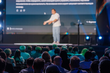 Speaker giving an engaging presentation to a seated audience at a conference. The audience is attentively listening and the atmosphere is professional.