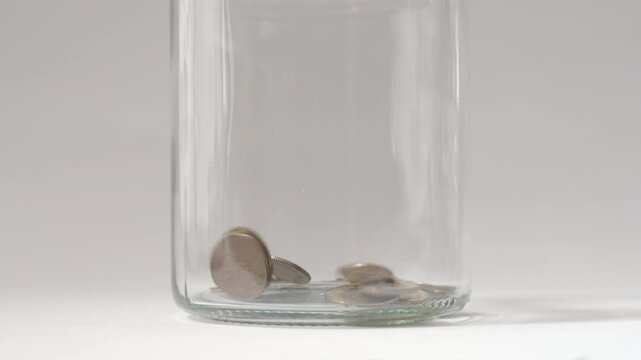 Coins inside a jar, many small golden coins fall into a glass jar for safekeeping. Gathering money.