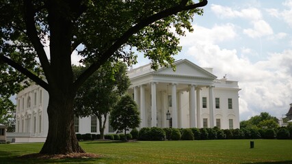 Angled view of the White House with green grass, trees cloudy blue sky in spring.
