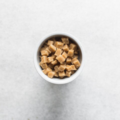 Overhead view of peanut butter fudge pieces in a white ceramic ramekin, top view of soft peanut fudge squares on a white background