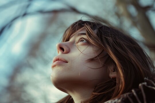 A woman looks upwards towards the sky, with a tree providing a natural backdrop