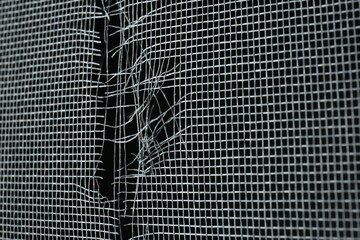 Torn window screen against black background, closeup