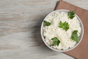 Tasty cooked rice with parsley in bowl on wooden table, top view. Space for text