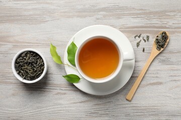 Refreshing green tea in cup, spoon and leaves on light wooden table, flat lay