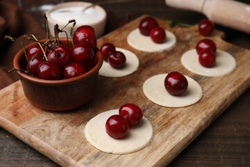 Process of making dumplings (varenyky) with cherries. Raw dough and ingredients on wooden table, closeup