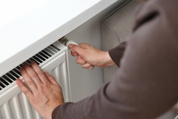 Man adjusting temperature of heating radiator indoors, closeup