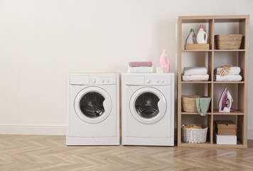 Two washing machines near beige wall in laundry room