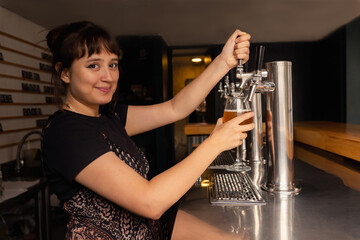 Portrait of waitress in profile filling a glass of beer from the tap.