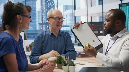 Insurance broker explaining financial plans to senior couple in a modern office, receiving expert advice on retirement plans. Discussing investment strategy, pension options and savings. Camera B.