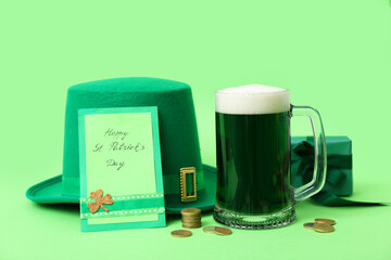 Glass of beer with greeting card, gift box, coins and leprechaun hat on green background. St....