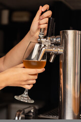 Female bartender's hand pouring beer from tap in a bar.