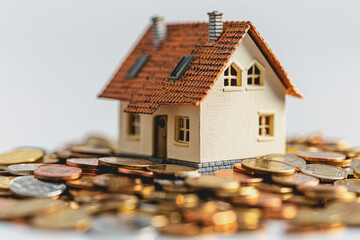 A small house resting on a pile of coins. on the table inside the house white background.