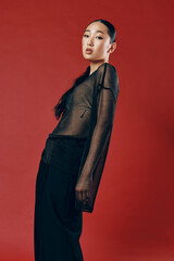 Fashion asian woman in sheer top and pants posing against a red background