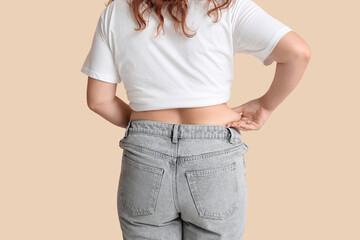Overweight woman in tight jeans on beige background, back view. Excess weight concept