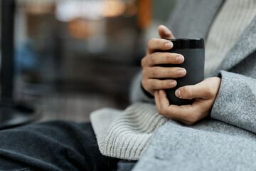 Fashion person in gray sweater and pants sitting in chair holding coffee cup