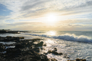 Sunset over the ocean, waves crashing on rocky shore