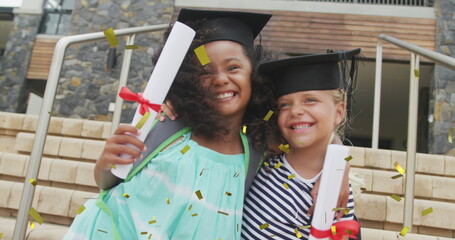 Image of gold confetti over happy diverse schoolgirls with diplomas and mortar boards embracing