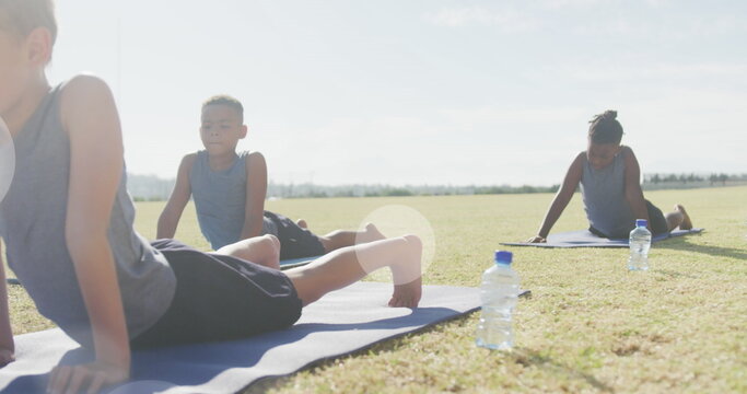 Image of light spots over happy diverse schoolboys stretching in outdoor yoga class - Powered by Adobe