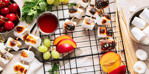 Marshmallow skewers and and strawberry, cherry, grame on light wooden background. Summer party food