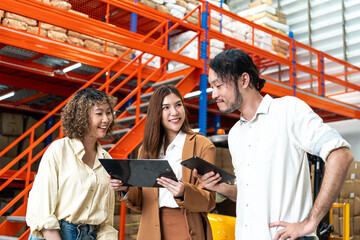 Diverse team discusses logistics in a warehouse, each holding a tablet, highlighting collaboration and technology in inventory management. - Powered by Adobe