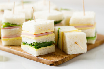 Sandwich of white soft bread with ham, cheese and lettuce on wooden board.