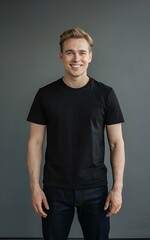 Obraz premium A young man standing against a gray background, wearing a black t-shirt and black pants. He is smiling and appears to be posing for the photo, t-shirt mockup.