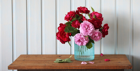 garden climbing pink and scarlet roses in a glass vase on the table in the cottage.
