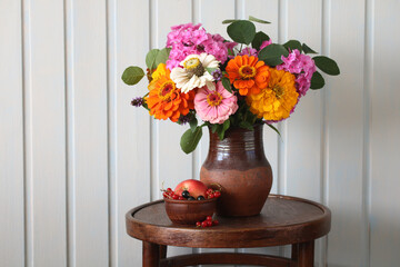bouquet of garden yellow and orange blue and pink phlox in a rural jug on a round table. copy space. rustic still life. flowers, fruits and berries.