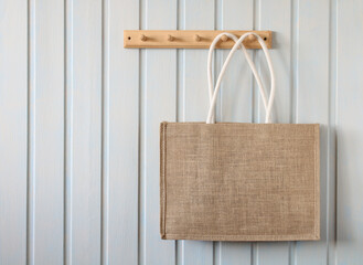 cloth bag hangs on a wooden hanger on a white board wall in the cottage. there is no plastic...