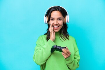 Young hispanic woman playing with a video game controller isolated on blue background shouting with...