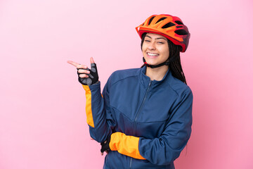 Teenager cyclist girl isolated on pink background pointing finger to the side