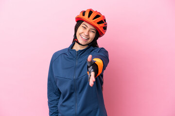 Teenager cyclist girl isolated on pink background shaking hands for closing a good deal