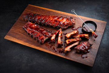 Barbecue spareribs St Louis cut with hot rub and BBQ sauce served as close-up on a wooden design cutting board