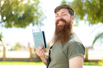 Fototapeta premium Redhead man with beard holding a passport at outdoors smiling a lot