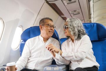 Obraz premium A mature couple enjoys a plane ride sitting near the window. They looked out into the sky. Immerse yourself in the scenery and excitement of the journey. To create precious memories together