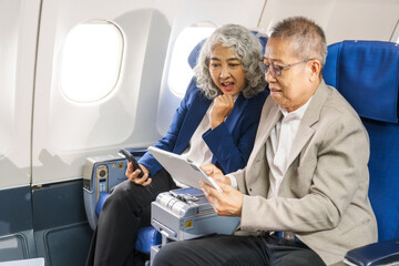 A mature couple enjoys a plane ride, seated near the window. They gaze out at the sky, savoring the view and the excitement of travel, creating cherished memories together.