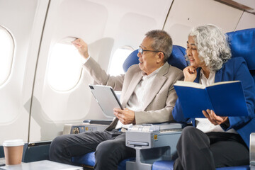 Naklejka premium A mature couple enjoys a plane ride, seated near the window. They gaze out at the sky, savoring the view and the excitement of travel, creating cherished memories together.