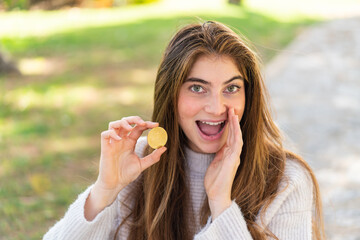 Young pretty caucasian woman holding a Bitcoin at outdoors shouting with mouth wide open