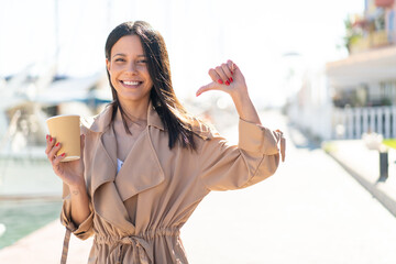Young woman at outdoors holding a take away coffee at outdoors proud and self-satisfied