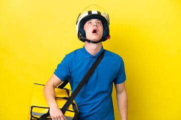 Young Brazilian man with thermal backpack isolated on yellow background looking up and with surprised expression