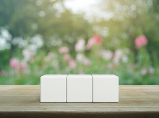 Three white block cubes on wooden table over blur pink flower and tree in garden