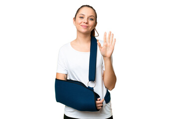 Young blonde woman with broken arm and wearing a sling over isolated chroma key background counting...
