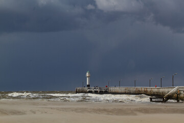 Dark sky and light variation on the beach facing an elegant wooden pier, North Sea high tide under windy conditions