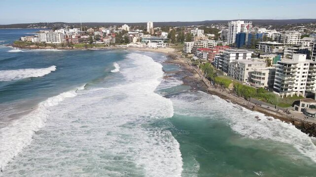 Aerial drone pullback reverse view from above Cronulla rock pools heading north along Prince Street and Cronulla beach in the Sutherland Shire, South Sydney, NSW Australia on a sunny morning on 14 Jul